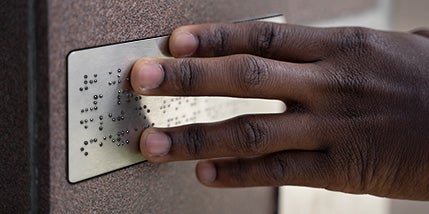 A Person’s Hand Reading The Braille On A Plastic Custom ADA Sign