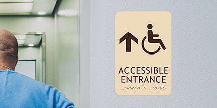 Tan ADA Accessible Entrance Sign With Black Text And Corresponding Braille Below