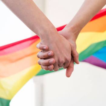 holding hands in front of rainbow flag