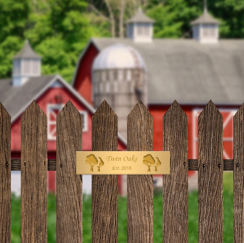 Engraved Brass Plate On A Picket Fence In Front Of A Barn Saying Twin Oaks, Established 2018