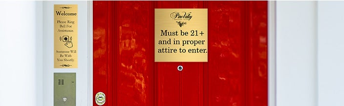 Custom engraved brass sign hanging on a front door that has a vineyard name with an age notice and a sign above the doorbell