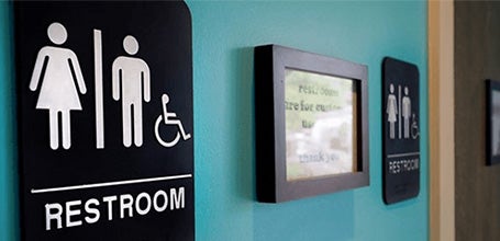 Black restroom signs with white text and symbols next to restroom doors