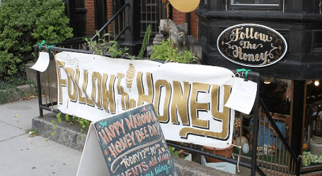 White banner with FOLLOW THE HONEY written in gold text hangs in front of a store